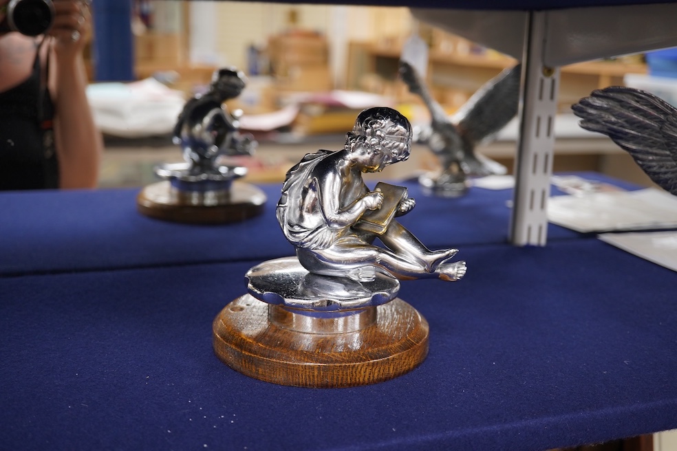 Two chrome car mascots, one in the form of an eagle stamped Finnigans London, wingspan 26cm, and the other of a classical child writing, mounted on a substantial radiator cap and oak base. Condition - fair to good, some